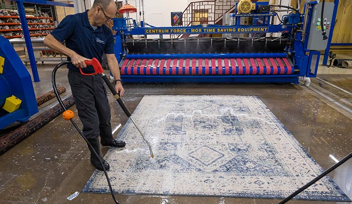 A professional using a high-pressure washer gun to clean a large patterned area rug