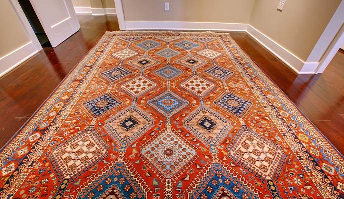 Large antique patterned area rug laid out on dark hardwood flooring