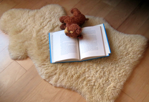 A teddy bear reading a book on a sheepskin wool rug