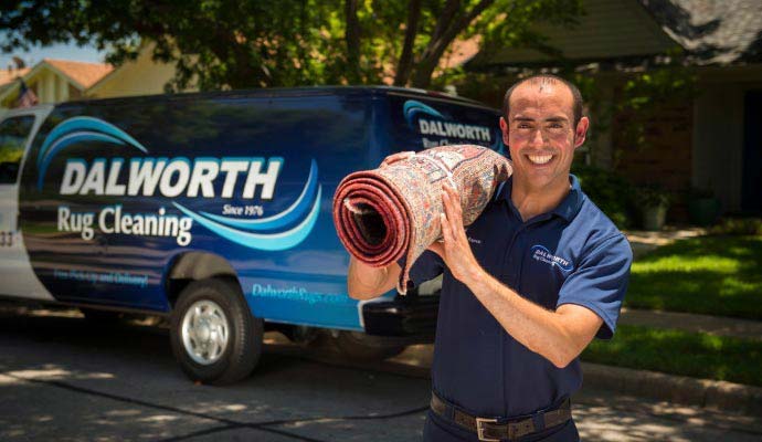 Professional rug cleaning technician holding a rolled rug in front of a service van