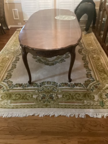 A large traditional dining room area rug with an ivory and green floral border medallion pattern, completely deep-cleaned, sanitised for pet odours, and pile-restored beneath a large wooden dining table.