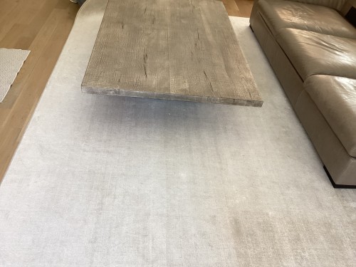 Large cream neutral area rug positioned underneath a wooden coffee table and leather sofa inspected for soil removal, furniture marks, and off-site rug cleaning.
