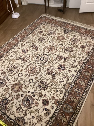 A large traditional Persian area rug with an intricate ivory field, floral medallion patterns, and a brown border, completely deep-cleaned, treated for colour bleeding, and pile-restored on a wood floor.