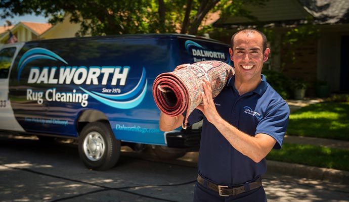 A smiling technician carrying a rolled area rug toward a branded service van for safe transport to our cleaning facility.