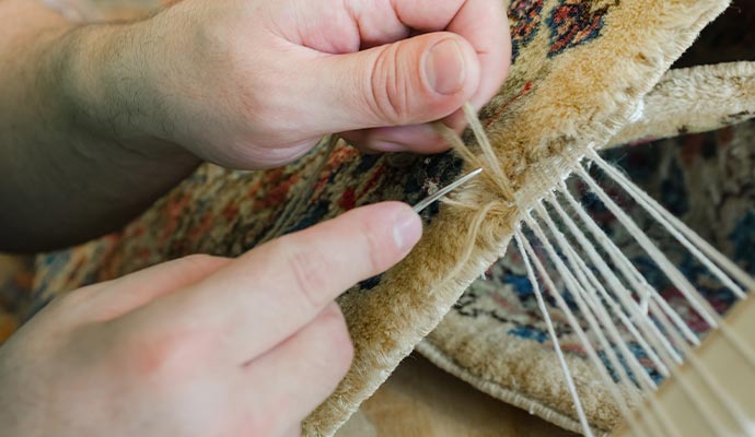 Technician weaving new yarn knots to patch a damaged section of a rug