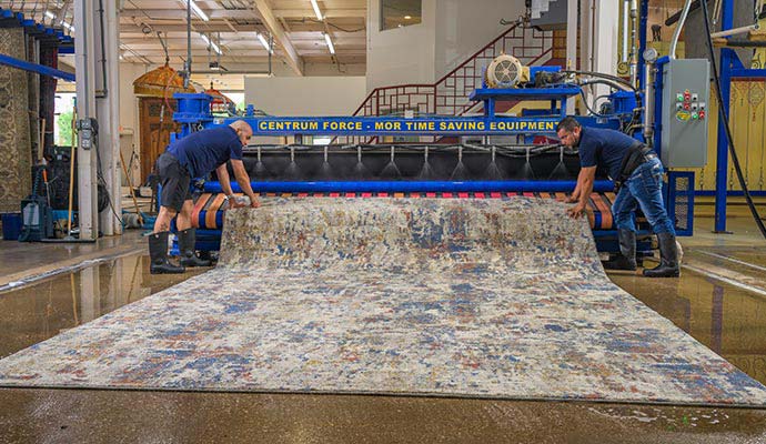 Two technicians washing a large area rug using specialized cleaning machinery