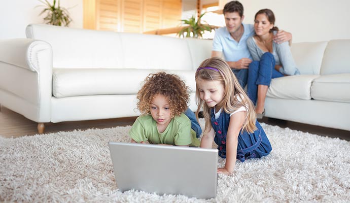 Two young children lying on a Flokati rug looking at a laptop
