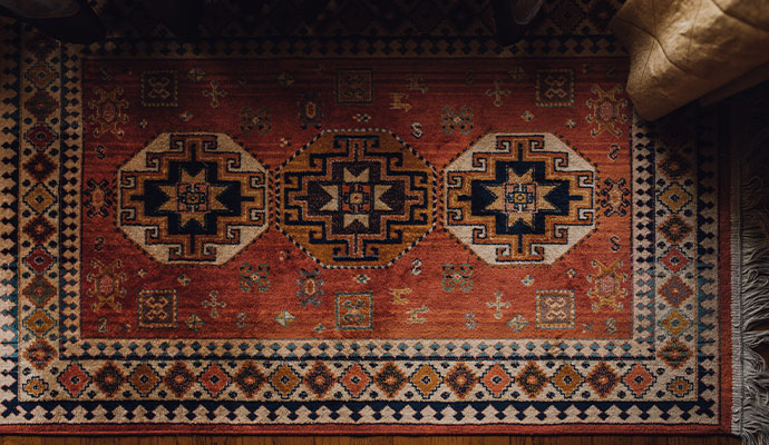 An overhead view of a clean red and orange patterned indoor area rug with tribal designs on a wood floor.