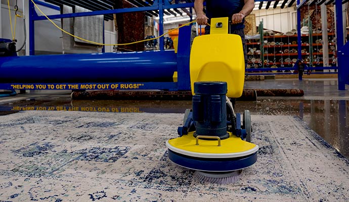 An industrial rug washing machine deep cleaning a blue and white patterned indoor rug to remove moisture and embedded dirt