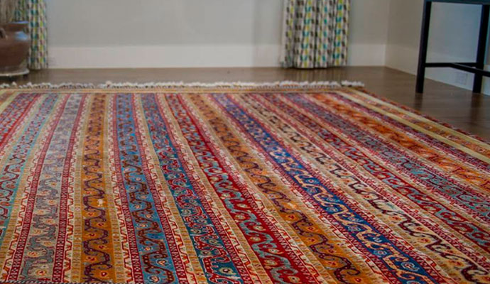 A close-up of a high-quality rug pad installed under a decorative red indoor rug for cushioning and floor protection.