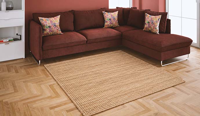 Natural woven jute area rug on parquet flooring in front of a sectional sofa